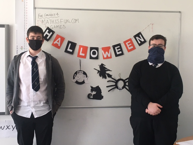 Two school pupils wearing face coverings, classroom, halloween creation stuck on white board